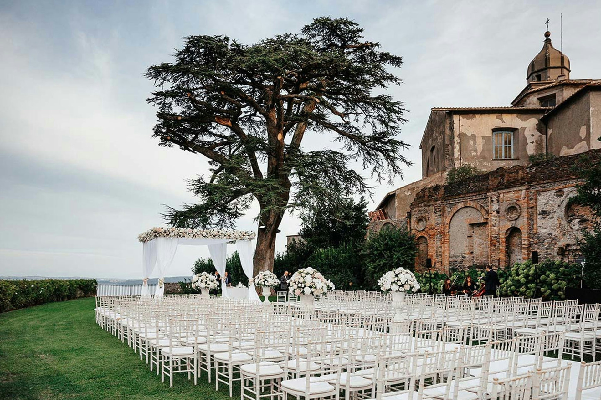 Outdoor ceremony set with white chairs beside a historic stone villa