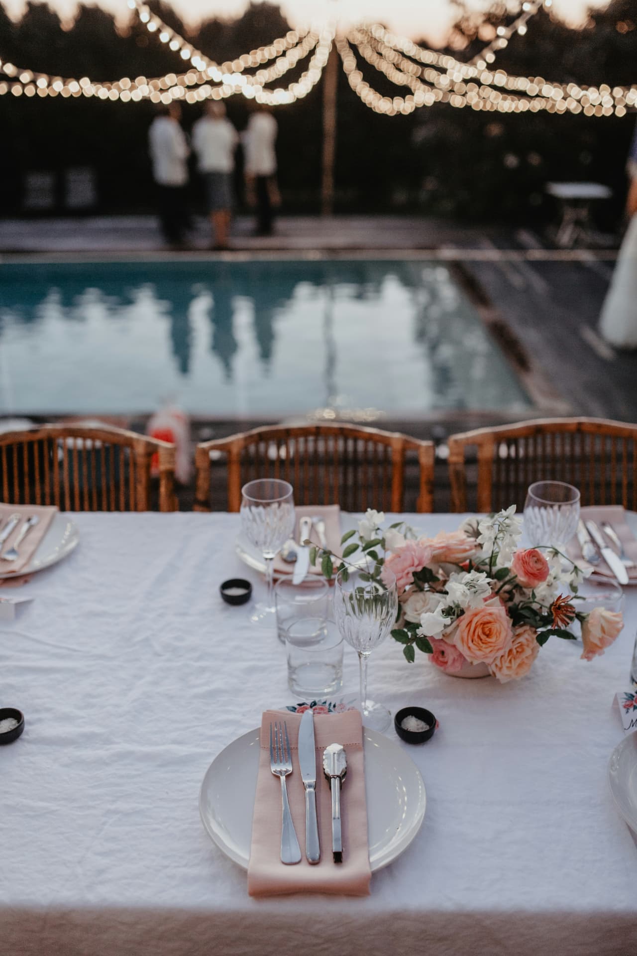 Poolside reception table set with linen, crystal and blush blooms at dusk